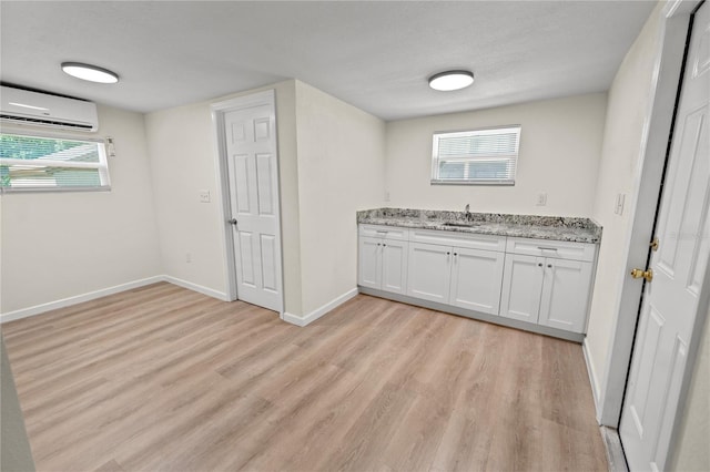 kitchen featuring sink, a textured ceiling, a wall unit AC, light stone countertops, and white cabinets