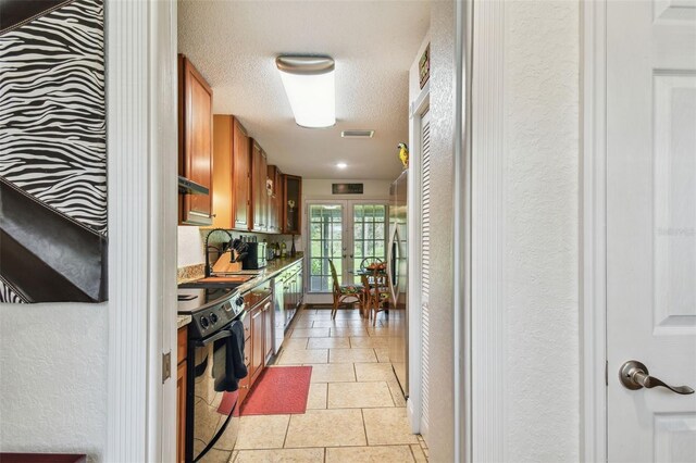 kitchen featuring stainless steel dishwasher, light tile patterned flooring, sink, stove, and a textured ceiling