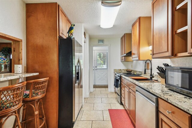 kitchen featuring light tile patterned floors, a textured ceiling, light stone countertops, appliances with stainless steel finishes, and sink