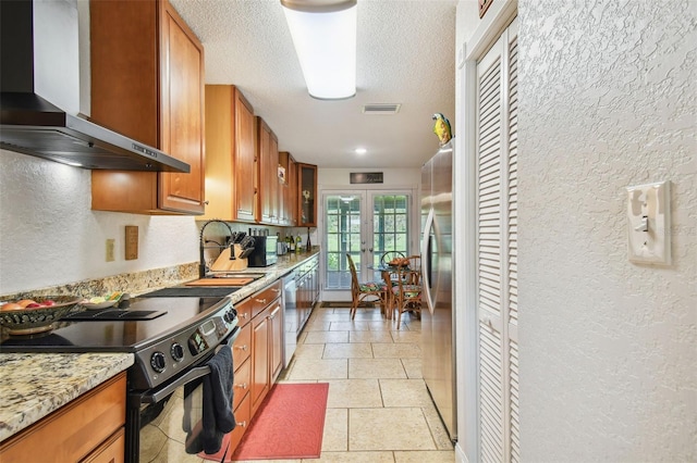 kitchen featuring wall chimney range hood, stainless steel appliances, french doors, light stone countertops, and light tile patterned floors