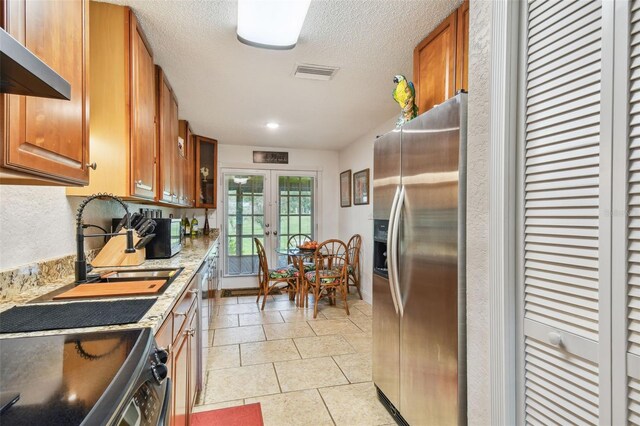 kitchen featuring french doors, light tile patterned floors, a textured ceiling, wall chimney exhaust hood, and appliances with stainless steel finishes