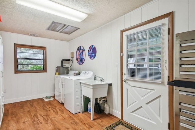 laundry area featuring light hardwood / wood-style flooring, electric water heater, a textured ceiling, wood walls, and separate washer and dryer