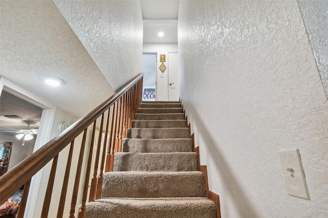 stairway featuring a textured ceiling and ceiling fan