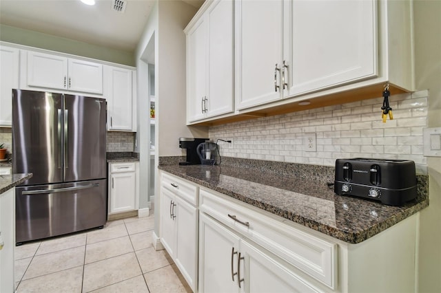 kitchen with dark stone counters, light tile patterned flooring, white cabinets, stainless steel fridge, and backsplash