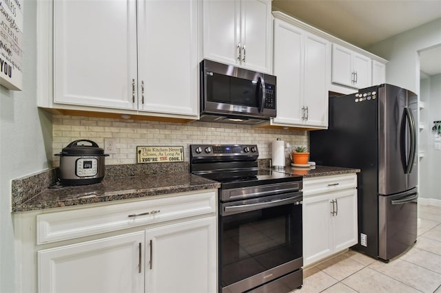 kitchen with white cabinetry, light tile patterned floors, dark stone counters, backsplash, and appliances with stainless steel finishes