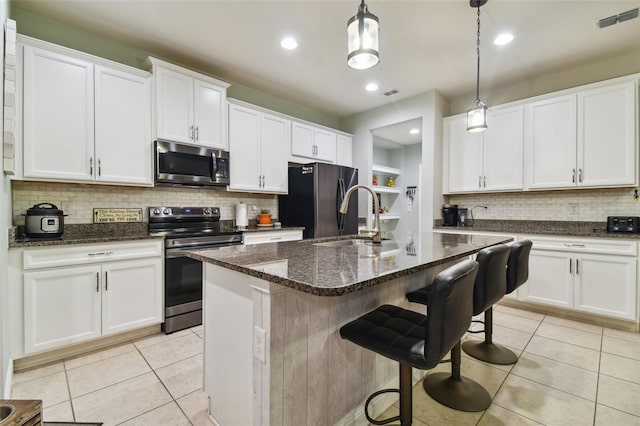 kitchen with light tile patterned flooring, electric range, backsplash, black fridge, and a center island with sink