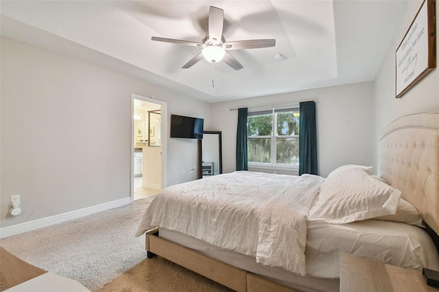 bedroom with ceiling fan, light colored carpet, ensuite bath, and a tray ceiling