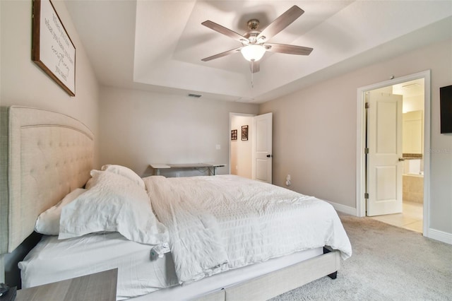 bedroom with light carpet, a raised ceiling, connected bathroom, and ceiling fan