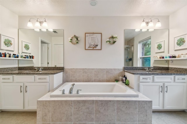 bathroom with tiled tub, tile patterned floors, a textured ceiling, and dual bowl vanity