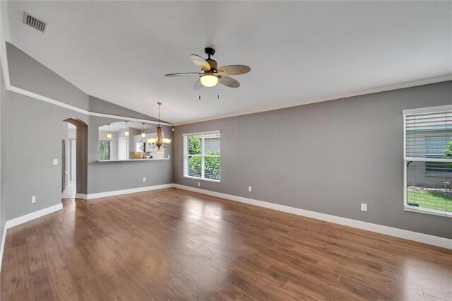 unfurnished living room with wood-type flooring, lofted ceiling, ceiling fan with notable chandelier, and crown molding