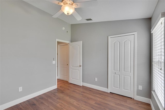 unfurnished bedroom with multiple windows, wood-type flooring, a closet, and ceiling fan