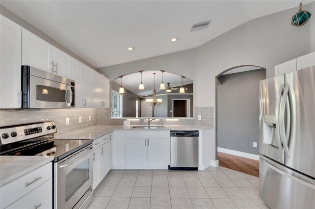 kitchen featuring stainless steel appliances, vaulted ceiling, white cabinetry, and decorative backsplash