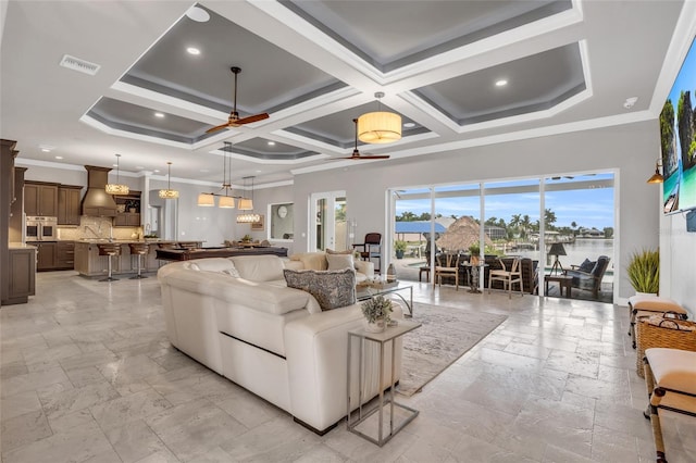 living room with ceiling fan, a high ceiling, coffered ceiling, a water view, and ornamental molding