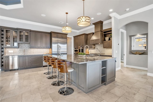 kitchen featuring decorative light fixtures, appliances with stainless steel finishes, custom range hood, a large island, and light stone countertops