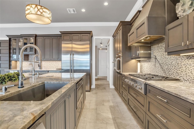 kitchen featuring sink, hanging light fixtures, ornamental molding, custom range hood, and light stone countertops