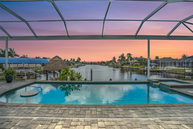 pool at dusk with a water view, an in ground hot tub, a lanai, and a patio area