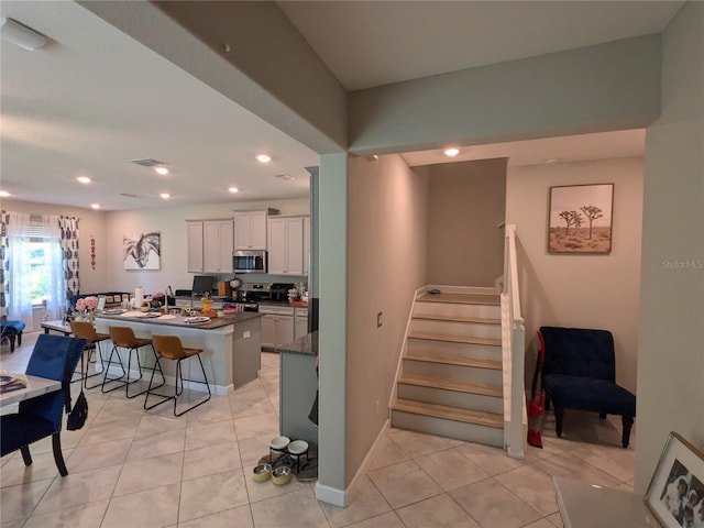 kitchen featuring a kitchen bar, light tile patterned floors, a center island, stainless steel appliances, and white cabinets