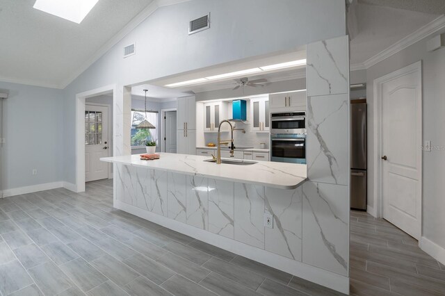 kitchen featuring appliances with stainless steel finishes, vaulted ceiling, sink, light stone counters, and ornamental molding