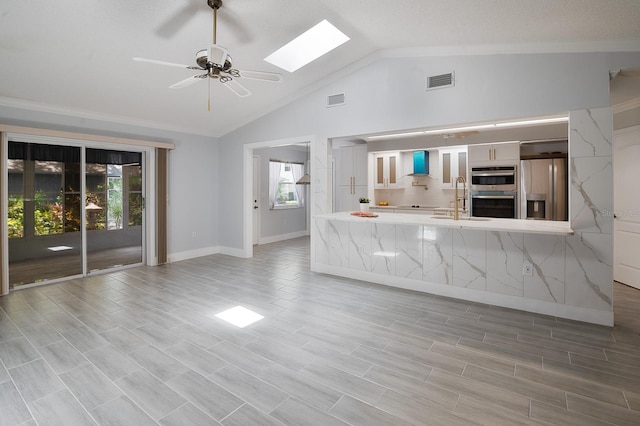 unfurnished living room with sink, vaulted ceiling with skylight, and ceiling fan