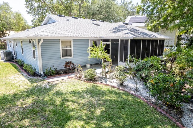 back of property with a sunroom, central AC, solar panels, and a lawn