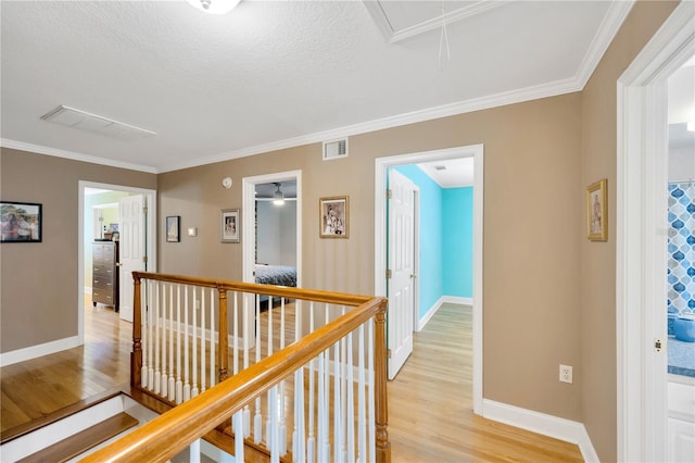 corridor with crown molding, a textured ceiling, and light wood-type flooring