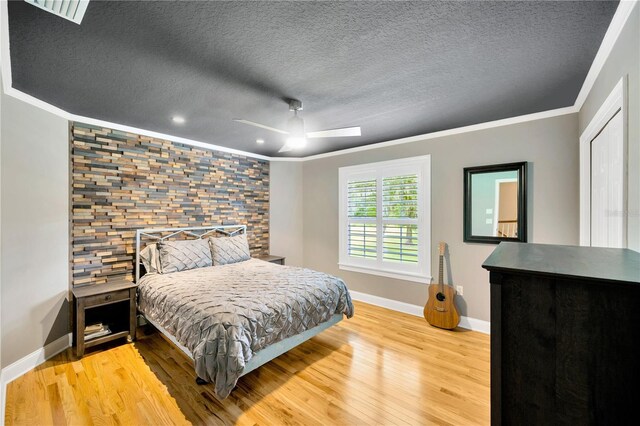 bedroom with crown molding, a textured ceiling, ceiling fan, and light wood-type flooring