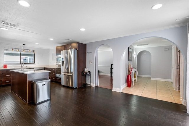 kitchen with sink, appliances with stainless steel finishes, dark brown cabinets, a center island, and light wood-type flooring