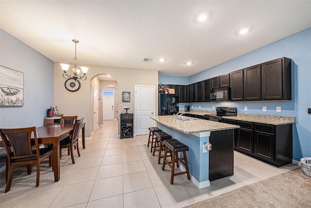 kitchen featuring decorative light fixtures, sink, light stone countertops, a center island with sink, and black appliances