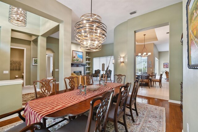 dining area with hardwood / wood-style flooring, a notable chandelier, a fireplace, and a tray ceiling