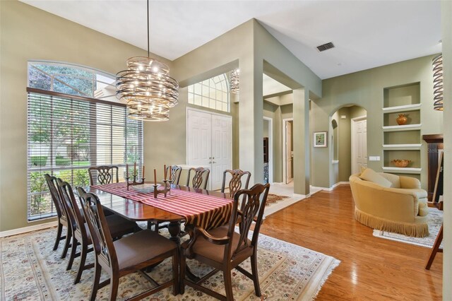 dining space featuring a chandelier, built in shelves, light wood-type flooring, and plenty of natural light