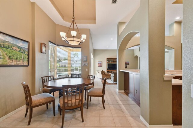 dining room featuring a raised ceiling, a high ceiling, light tile patterned floors, and an inviting chandelier