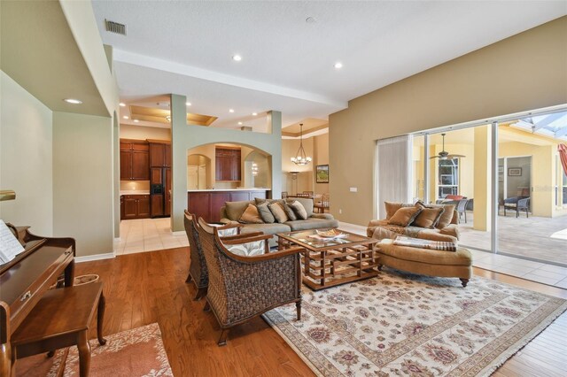 living room with light wood-type flooring and ceiling fan with notable chandelier