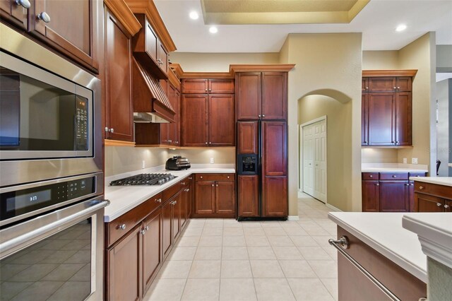 kitchen with built in appliances, light tile patterned floors, a raised ceiling, and custom range hood