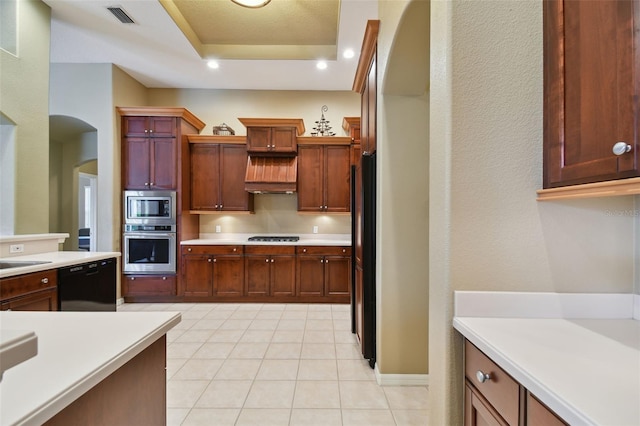 kitchen featuring premium range hood, black appliances, light tile patterned floors, and a tray ceiling