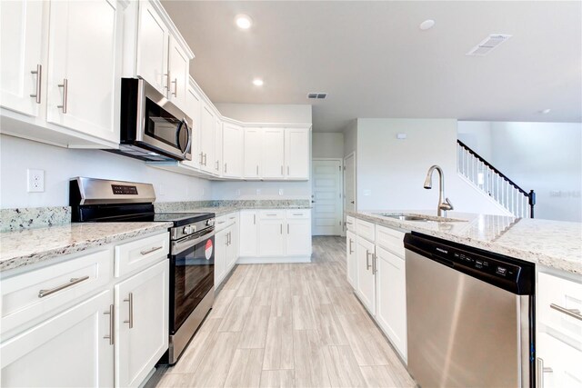 kitchen featuring sink, stainless steel appliances, light stone countertops, white cabinets, and light wood-type flooring