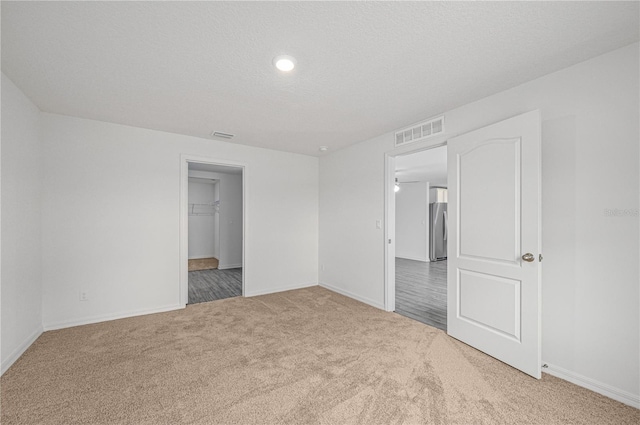 unfurnished bedroom with carpet, a textured ceiling, and stainless steel fridge