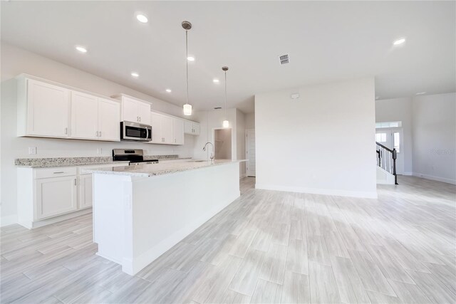 kitchen featuring a center island with sink, stainless steel appliances, hanging light fixtures, and white cabinets