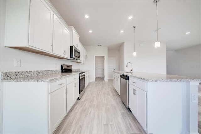 kitchen with appliances with stainless steel finishes, decorative light fixtures, white cabinetry, light stone countertops, and a center island with sink