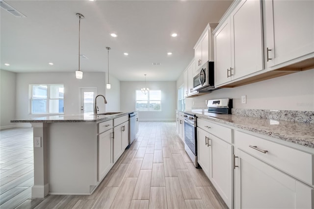 kitchen featuring pendant lighting, sink, appliances with stainless steel finishes, white cabinets, and a center island with sink