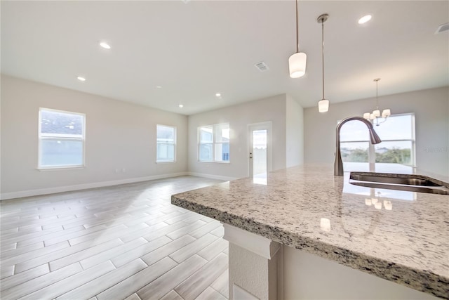 kitchen featuring sink, hanging light fixtures, a notable chandelier, light hardwood / wood-style floors, and light stone countertops