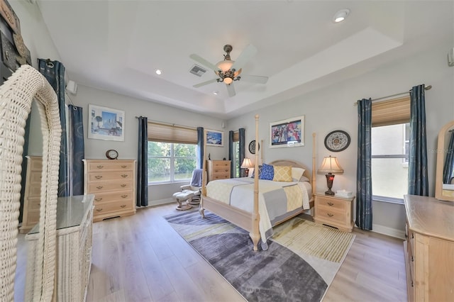 bedroom with light wood-type flooring, ceiling fan, and a tray ceiling