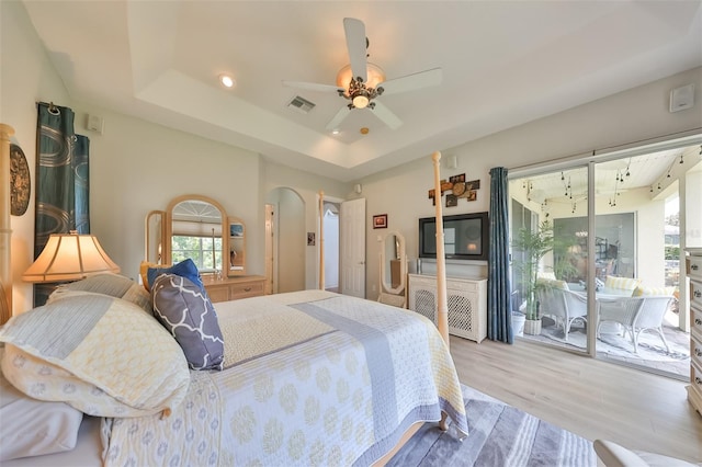 bedroom with a tray ceiling, access to outside, light hardwood / wood-style floors, and ceiling fan