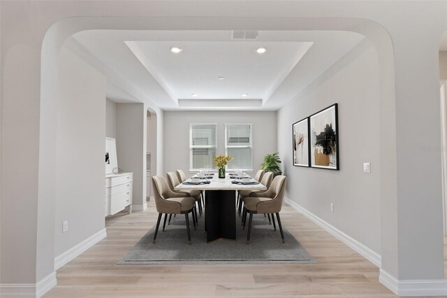 dining space with light hardwood / wood-style floors and a tray ceiling