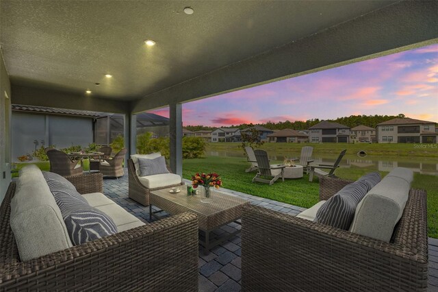 patio terrace at dusk with a lawn, a water view, and an outdoor hangout area