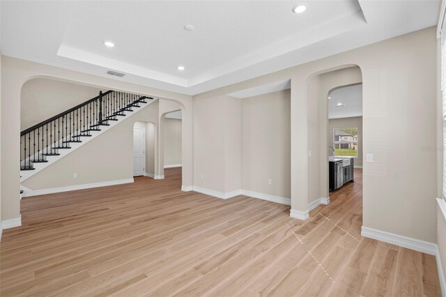 unfurnished living room with light wood-type flooring, a raised ceiling, and sink