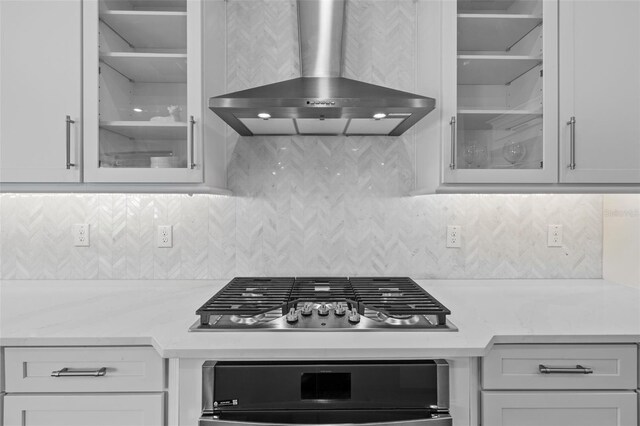 kitchen featuring decorative backsplash, white cabinets, oven, stainless steel gas stovetop, and wall chimney range hood