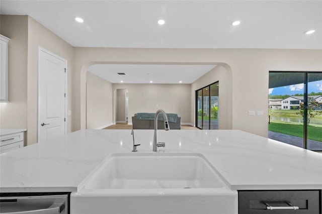 kitchen with dishwasher, sink, white cabinetry, a center island with sink, and light stone countertops