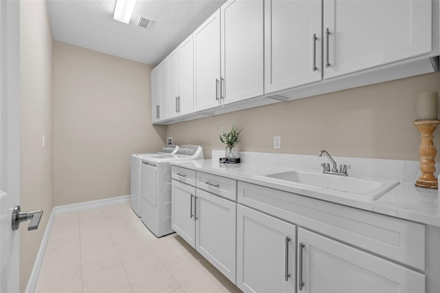 washroom with a textured ceiling, washing machine and dryer, sink, and cabinets