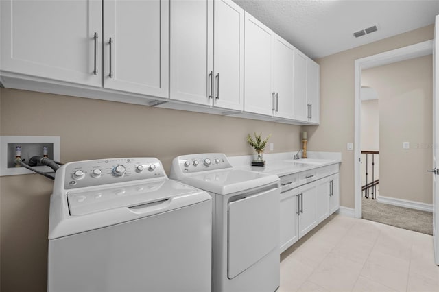 clothes washing area with sink, a textured ceiling, washer and clothes dryer, cabinets, and light colored carpet