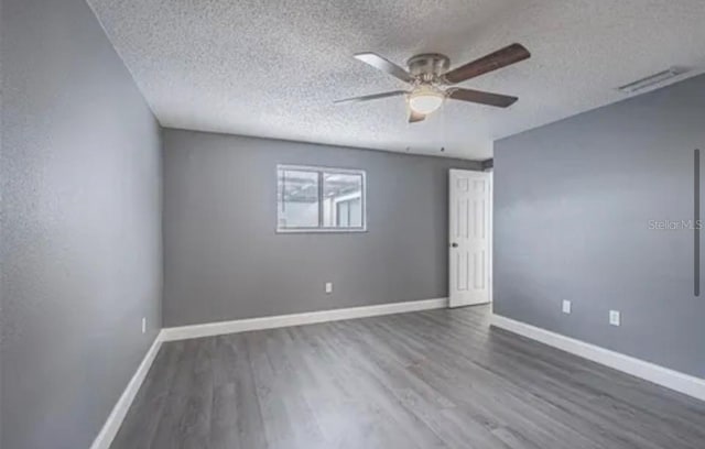 unfurnished room with visible vents, ceiling fan, a textured ceiling, wood finished floors, and baseboards